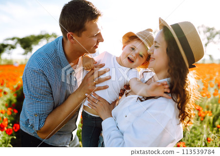 Family with a child walking on a poppy field. Mother, father, little daughter having fun on the poppy field. Family with a child walking on a poppy field. Mother, father, little daughter having fun on the poppy field. 113539784