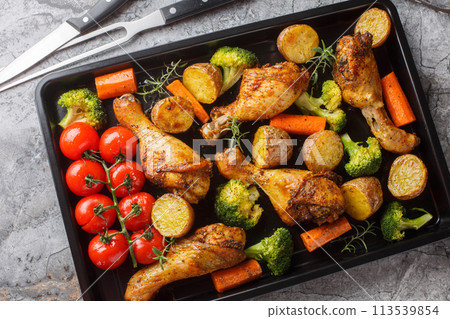 Tasty Baked ruddy chicken legs with potatoes, broccoli, tomato, carrot close-up on a baking sheet. Horizontal top view Tasty Baked ruddy chicken legs with potatoes, broccoli, tomato, carrot close-up on a baking sheet. Horizontal top view 113539854