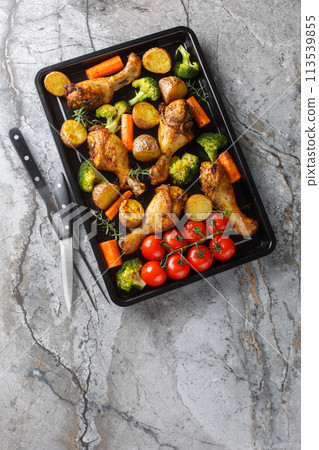 Homemade baked chicken drumsticks with vegetables and rosemary close-up on a baking sheet. Vertical top view 113539855