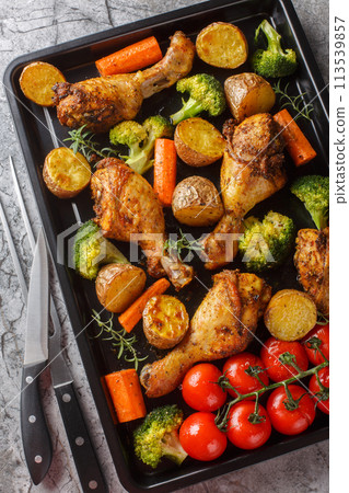 Healthy food baked chicken drumstick with broccoli, potatoes, tomatoes and carrots close-up on a sheet pan. Vertical top view Healthy food baked chicken drumstick with broccoli, potatoes, tomatoes and carrots close-up on a sheet pan. Vertical top view 113539857