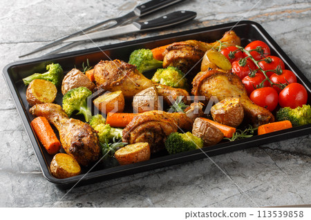 Oven baked chicken drumsticks with fresh baked vegetables close-up on a baking sheet. Horizontal Oven baked chicken drumsticks with fresh baked vegetables close-up on a baking sheet. Horizontal 113539858