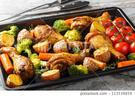 Tasty Baked ruddy chicken legs with potatoes, broccoli, tomato, carrot close-up on a baking sheet. Horizontal Tasty Baked ruddy chicken legs with potatoes, broccoli, tomato, carrot close-up on a baking sheet. Horizontal 113539859