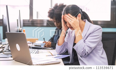Overworked businesswoman sitting with head in hands at laptop desk in office Overworked businesswoman sitting with head in hands at laptop desk in office 113539871