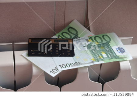 A calculator and one hundred euro banknotes lie on the radiator of the heating system, A calculator and one hundred euro banknotes lie on the radiator of the heating system, 113539894