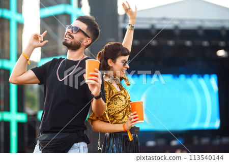 Lovely couple having fun at festival. Young friends with beer at beach party. Summer holiday, vacation. Lovely couple having fun at festival. Young friends with beer at beach party. Summer holiday, vacation. 113540144