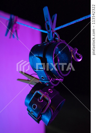 bdsm leather handcuffs hanging on a clothesline in neon light on a black background bdsm leather handcuffs hanging on a clothesline in neon light on a black background 113542322
