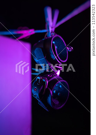 bdsm leather handcuffs hanging on a clothesline in neon light on a black background bdsm leather handcuffs hanging on a clothesline in neon light on a black background 113542323