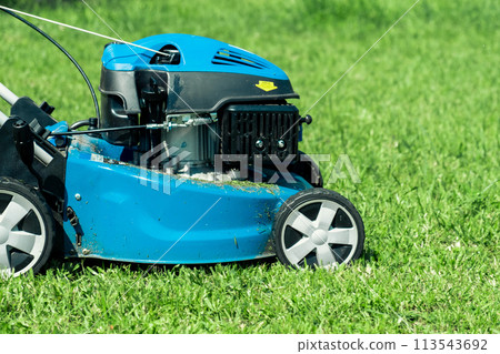 Lawn mower cutting grass. Small grass cuttings fly out of lawnmower. Grass clippings get spewed out of a mower pushed around by landscaper. CloseUp. Gardener working with mower machine. Mowing lawns Lawn mower cutting grass. Small grass cuttings fly out of lawnmower. Grass clippings get spewed out of a mower pushed around by landscaper. CloseUp. Gardener working with mower machine. Mowing lawns 113543692