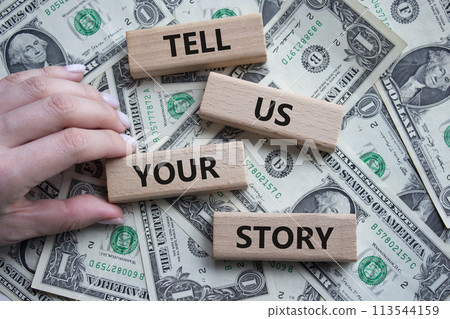 Tell us your story symbol. Concept words Tell us your story on wooden blocks. Beautiful dollar background. Businessman hand. Business and Tell us your story concept. Copy space. 113544159