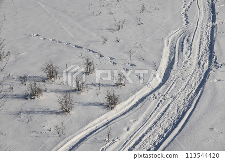 Deserted winter landscape. A path of footprints stretches across the pure white snow Deserted winter landscape. A path of footprints stretches across the pure white snow 113544420