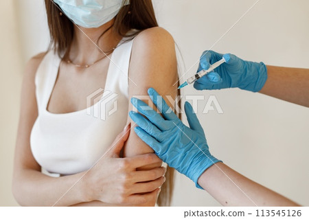 Young woman wearing mask and receiving coronavirus vaccine. A young girl receiving an immunity shot in the forearm. Closeup of doctor in blue gloves giving Covid-19, AIDS or flu antivirus vaccine to 113545126