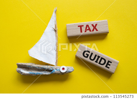 Tax Guide symbol. Concept word Tax Guide on wooden blocks. Beautiful yellow background with boat. Business and Tax Guide concept. Copy space Tax Guide symbol. Concept word Tax Guide on wooden blocks. Beautiful yellow background with boat. Business and Tax Guide concept. Copy space 113545273