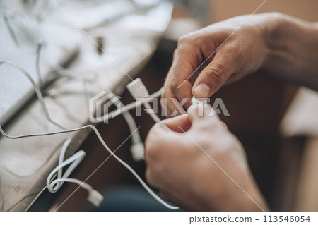 Entangled Solutions - A close-up of hands meticulously selecting the right cable from a tangled assortment, symbolizing the complexity and precision needed in technological troubleshooting 113546054