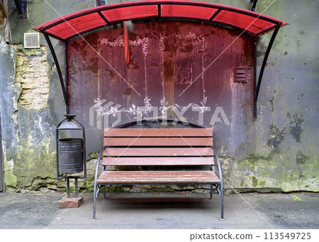 A bench near an old peeling green-blue wall, painted red with light through a red visor 113549725
