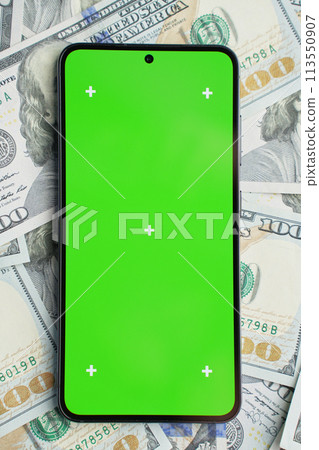 Smartphone with green screen on pile of dollar banknotes, top view 113550907