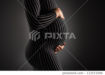 Elegant Pregnant Woman Embracing Her Belly in Striped Dress 113551099