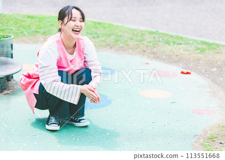 A nursery teacher playing with a child in front of the playground equipment in the park A nursery teacher playing with a child in front of the playground equipment in the park 113551668