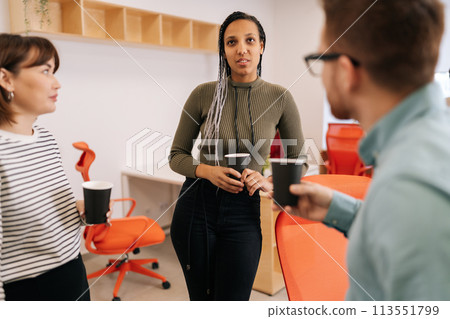 Selective focus of diverse young male and female office colleagues having conversation during coffee break at workplace. Multiethnic coworkers discuss issues during coffee break and share opinions 113551799