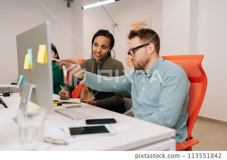 Skilled male leader in eyeglasses helping new African female worker with computer corporate software application in office. Motivated young mixed race employees developing project growth strategy 113551842