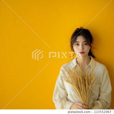Beautiful woman holding ears of rice in front of a yellow background 113552067