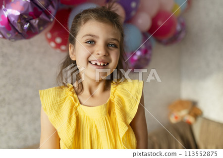 Laughing real girl 7 years old in yellow dress against backdrop of festive balloons in holiday at home Laughing real girl 7 years old in yellow dress against backdrop of festive balloons in holiday at home 113552875