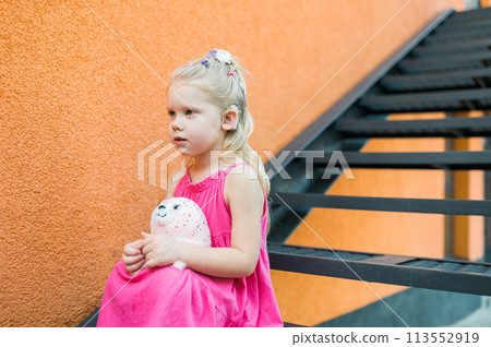 Child girl with hearing aid cochlear implant in pink dress having fun on summer street. Aid for the treatment of deafness and hearing loss in humans. Copy space 113552919