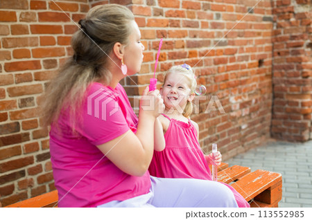 Blonde little girl with cochlear implant playing with her mother outdoor. Hear impairment deaf and health concept. Diversity and inclusion. Copy space 113552985