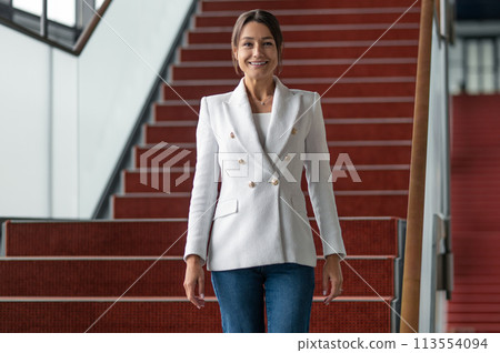Pretty business woman in white jacket going down the stairs Pretty business woman in white jacket going down the stairs 113554094