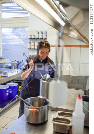 Young woman cooking soup in the kitchen and holding a ladle in hands 113554177