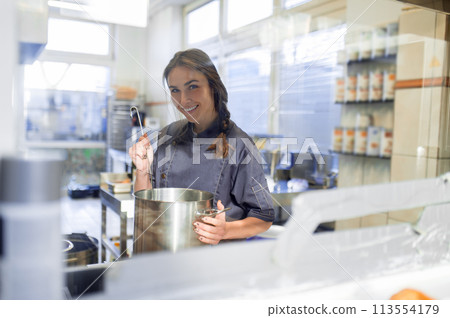 Young woman cooking soup in the kitchen and holding a ladle in hands 113554179