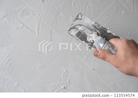 Applying decorative putty. White abstract texture of surface covered with putty. textured background of filler paste applied with putty knife in irregular dashes and strokes. Rough surface plaster 113554574
