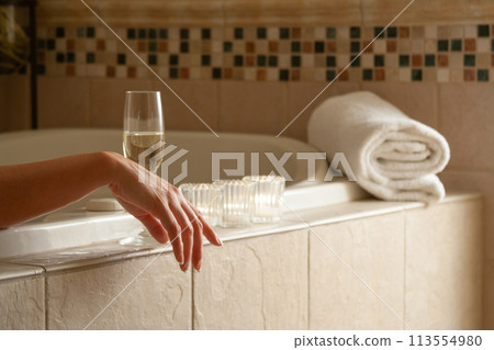 Woman Relaxing in the Bathroom Spa Tub with a Glass of Sparkling Champagne and Candles. 113554980