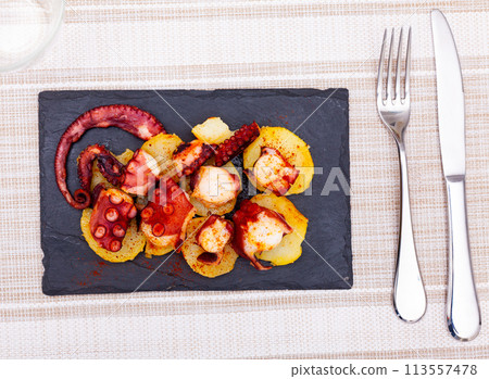 Boiled octopus tentacles with smoked paprika and potatoes on slate board 113557478
