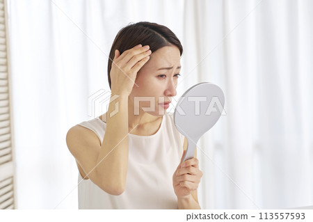 A woman in her 40s worries about her hair in the mirror A woman in her 40s worries about her hair in the mirror 113557593