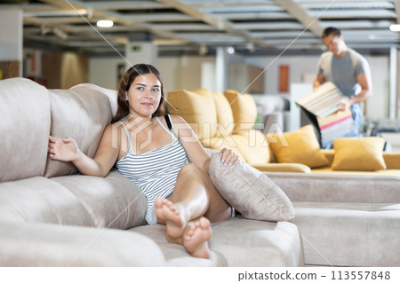 In furniture store,young girl is sitting on sofa with ottoman In furniture store,young girl is sitting on sofa with ottoman 113557848