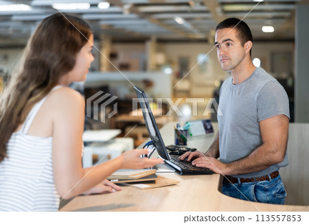 Male consultant stands near computer and explains to female buyer advantages of buying sofa 113557853