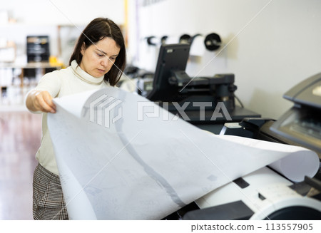 Female employee of the printing house checks the quality of the print Female employee of the printing house checks the quality of the print 113557905