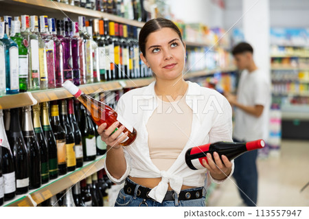 Young woman choosing bottle of wine for herself in supermarket Young woman choosing bottle of wine for herself in supermarket 113557947