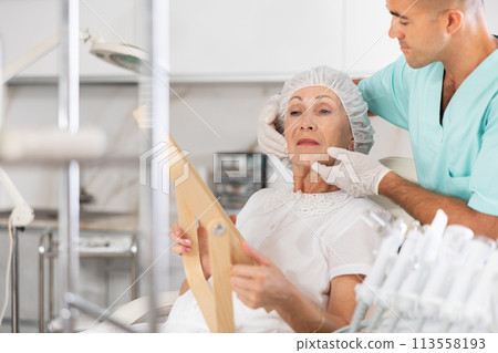 Man beautician examining face skin of female patient after cosmetology procedure in clinic 113558193