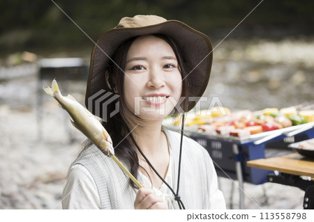 一位年輕女子在露營地吃鹽烤香魚的燒烤形象 113558798