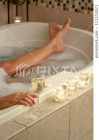 Woman Relaxing in the Bathroom Spa Tub with a Glass of Sparkling Champagne and Candles. 113558821