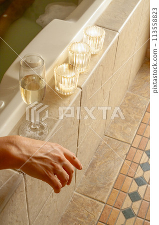 Woman Relaxing in the Bathroom Spa Tub with a Glass of Sparkling Champagne and Candles. 113558823