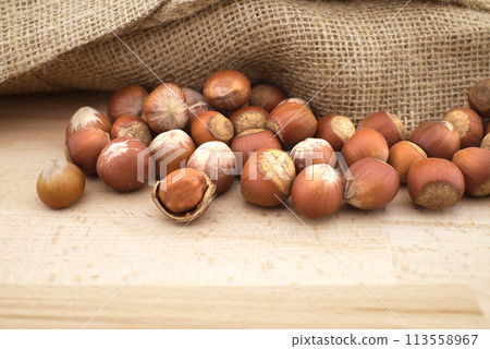 Hazelnuts beside the jute sack on wooden table 113558967
