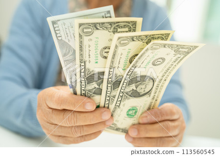 Asian senior woman holding and counting US dollar banknotes money in purse. Poverty, saving problem in retirement. 113560545