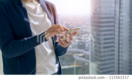 一位女士正在操作智慧型手機，背景是一座城市 113561517