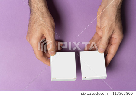 Male hand holding two pills box for compairing in front of purple background mock-up series Male hand holding two pills box for compairing in front of purple background mock-up series 113563800