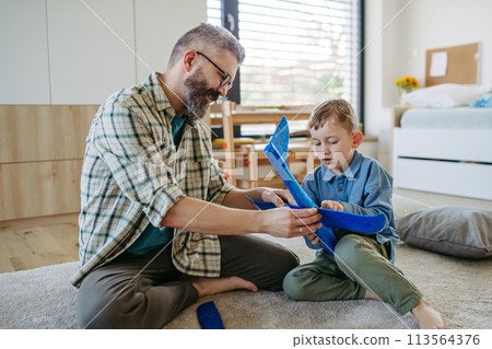 Playing with lightweight styrofoam planes. Playful father and son throwing and flying foam glider planes. Fathers day concept. 113564376