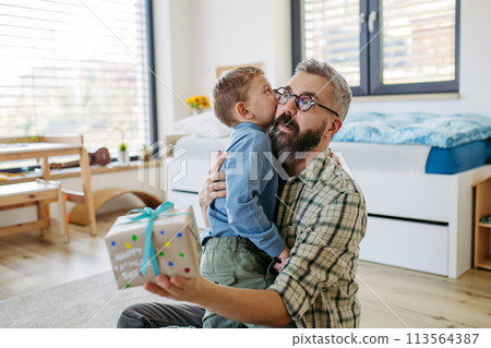 Dad get a handmade gift from little son, present wrapped in diy homemade wrapping paper. Father embracing boy. Happy Fathers day concept. Dad get a handmade gift from little son, present wrapped in diy homemade wrapping paper. Father embracing boy. Happy Fathers day concept. 113564387