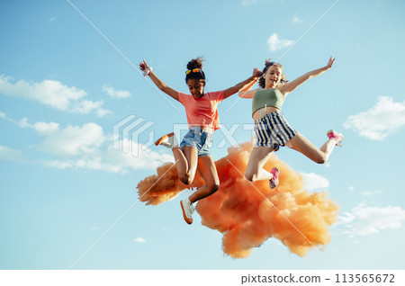 Young teenager girls friends jumping high. Having fun outdoors in city, standing on concrete wall. 113565672