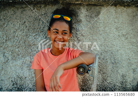 Teenager girl with skateboard spending time outdoors in city during warm summer holiday day. 113565680